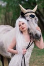 Attractive young woman in a white dress, standing on the green meadow near beautiful white horse Royalty Free Stock Photo