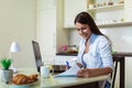 Young woman working with laptop computer and documents while sitting at the kitchen Royalty Free Stock Photo