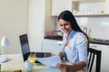 Young woman working with laptop computer and documents while sitting at the kitchen Royalty Free Stock Photo