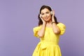 Attractive young woman in yellow dress looking camera, listen music, putting hands on headphones isolated on pastel Royalty Free Stock Photo