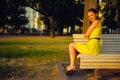 Attractive young woman in yellow dress, sitting in a summer park on a bench Royalty Free Stock Photo