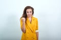 Attractive young woman in yellow jacket looking angry, holding fist, threatening