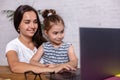 Attractive young woman and her little cute daughter are sitting at the table and having fun while doing homework Royalty Free Stock Photo