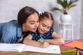 Attractive young woman and her little cute daughter are sitting at the table and having fun while doing homework Royalty Free Stock Photo