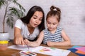 Attractive young woman and her little cute daughter are sitting at the table and having fun while doing homework Royalty Free Stock Photo