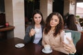 Attractive young women making selfie in restairant. Women drin cappuccino on terrace. Two female make photo together Royalty Free Stock Photo