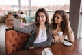 Attractive young women making selfie in restairant. Women drin cappuccino on terrace. Two female make photo together Royalty Free Stock Photo