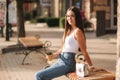 Attrective brunette sitting alone on the bench in centre of the city. Beautiful young woman drinking coffe outdoors. End Royalty Free Stock Photo