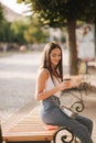 Attrective brunette sitting alone on the bench in centre of the city. Beautiful young woman drinking coffe outdoors. End Royalty Free Stock Photo