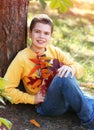 ÃÂ¡aucasian teenager boy dreams with smiling of good things in a yellow long sleeve shirt and blue jeans sitting near a tree in a