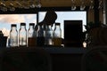 Bottles of syrup mixes on bar in front of silhouette of barman back-lit by daylight through window