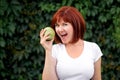 Beautiful young woman holding big green apple. Woman with open mouth ready to bite fresh apple outdoors. Green background Royalty Free Stock Photo