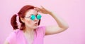 Beautiful young woman in pink shirt and blue round sunglasses looking for something, holding palm near forehead like sun visor. Royalty Free Stock Photo