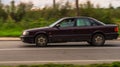 Audi 100 (C4) in motion on the country road. Purple car with old man driver, driving fast on the rural way, side view