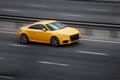 Audi yellow rides on the road. Against a background of blurred trees