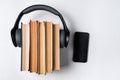 Audio book concept. Headphones worn on a stack of old books and mobile phone. White background, copy space top view Royalty Free Stock Photo