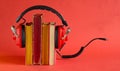 audio book concept with row of books,and vintage headphones, cable and audio plug, red background, free copy space Royalty Free Stock Photo