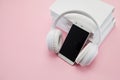 Audio books concept. Headphones and smartphone on a stack of white books over a pink background. Royalty Free Stock Photo