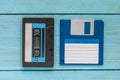 An audio cassette in a black plastic case and a blue floppy disk lie on a blue wooden background Royalty Free Stock Photo