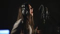 Audio recording studio. Woman with headphones and studio microphone singing.
