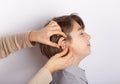 Audiologist fitting hearing aid on a smilling young boy`s ear