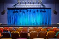 The auditorium in the theater. Blue-green curtain on the stage. Multicolored spectator chairs. Lighting equipment Royalty Free Stock Photo