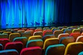 The auditorium in the theater. Blue-green curtain on the stage. Multicolored spectator chairs. Lighting equipment Royalty Free Stock Photo