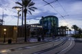 Audubon Aquarium with train tracks in the street and lush green palm trees along the riverfront with clouds at sunset