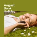 August bank holiday text on green with happy caucasian woman lying on grass in sun on smartphone Royalty Free Stock Photo
