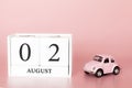 August 02nd. Day 2 of month. Calendar cube on modern pink background with car