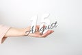 August 15th. Day 15 of month, Calendar date. Calendar Date floating over female hand on grey background. Summer month, day of the