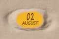 August 2. 2th day of the month, calendar date. Hole in sand. Yellow background is visible through hole