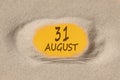 August 31. 31th day of the month, calendar date. Hole in sand. Yellow background is visible through hole