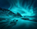 Aurora borealis above snowy mountain and sandy beach with stones