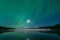 Aurora borealis, Northern green lights with full moon and stars in the night sky over misty mountain lake, mirrored reflection in Royalty Free Stock Photo