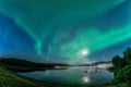 Aurora borealis, Northern green lights with full moon and stars in the night sky over mountain lake, mirrored reflection in water