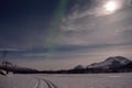 Aurora borealis, northern light over a frozen snowy river bed with full moon Royalty Free Stock Photo