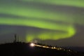 Aurora Borealis over hill with antennas and car with lights on