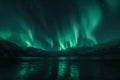 Aurora borealis over mountain peak reflected in sea lake waters at night. Beautiful winter landscape with aurora lights Royalty Free Stock Photo