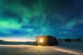 Aurora borealis over old small house with yellow light in window