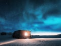 Aurora borealis over old small house with yellow light in window