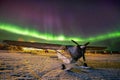 Aurora borealis over a small airplane on a frozen lake.