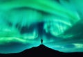 Aurora borealis and silhouette of a man on the mountain peak