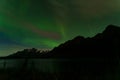 the aurora lights above water and mountains in the distance with trees in foreground Royalty Free Stock Photo
