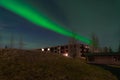 Aurora lights shine over a house atop a grassy hill