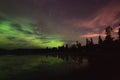 Aurora reflecting of a lake, city lights lighting up clouds - Camera in forground