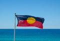 Australian aboriginal flag waving with blue sky and ocean water at the background. Royalty Free Stock Photo