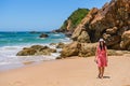 Australian coast, a young woman in a hat and pink dress walks on the sandy beach between large rocks on the coast Royalty Free Stock Photo