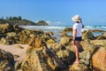 Australian coast, a young woman in a hat, T-shirt and shorts stands on the rocks on the beach and looks at the seaside landscape Royalty Free Stock Photo