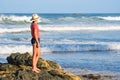 Australian coast, a young woman in a hat,T-shirt and shorts stands on the rocks on the beach and looks towards the sea Royalty Free Stock Photo